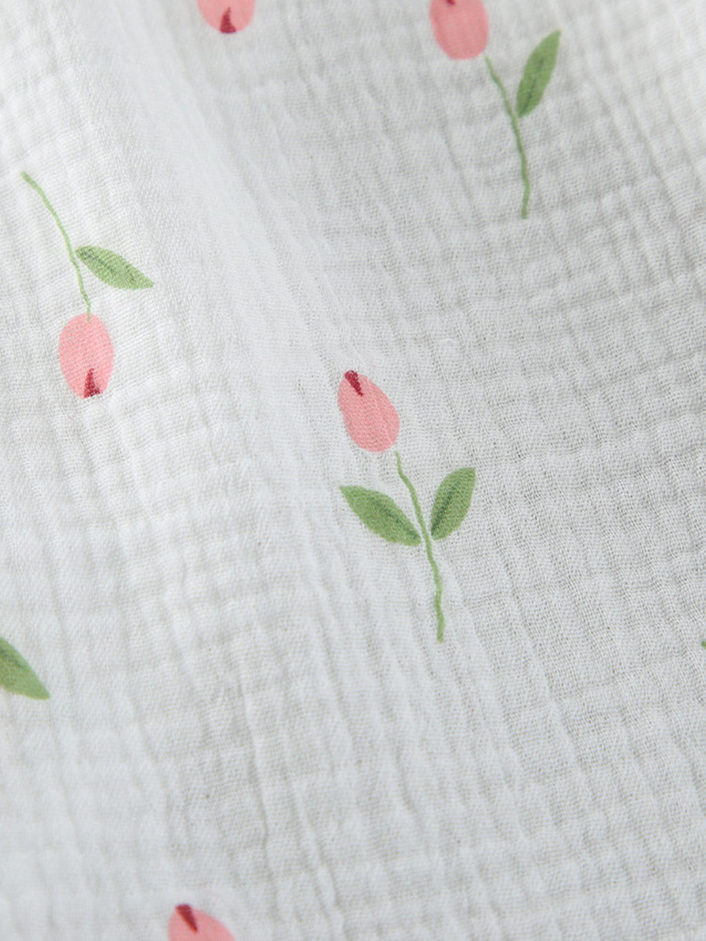 Close up of white fabric with a floral print of pink tulips and green leaves