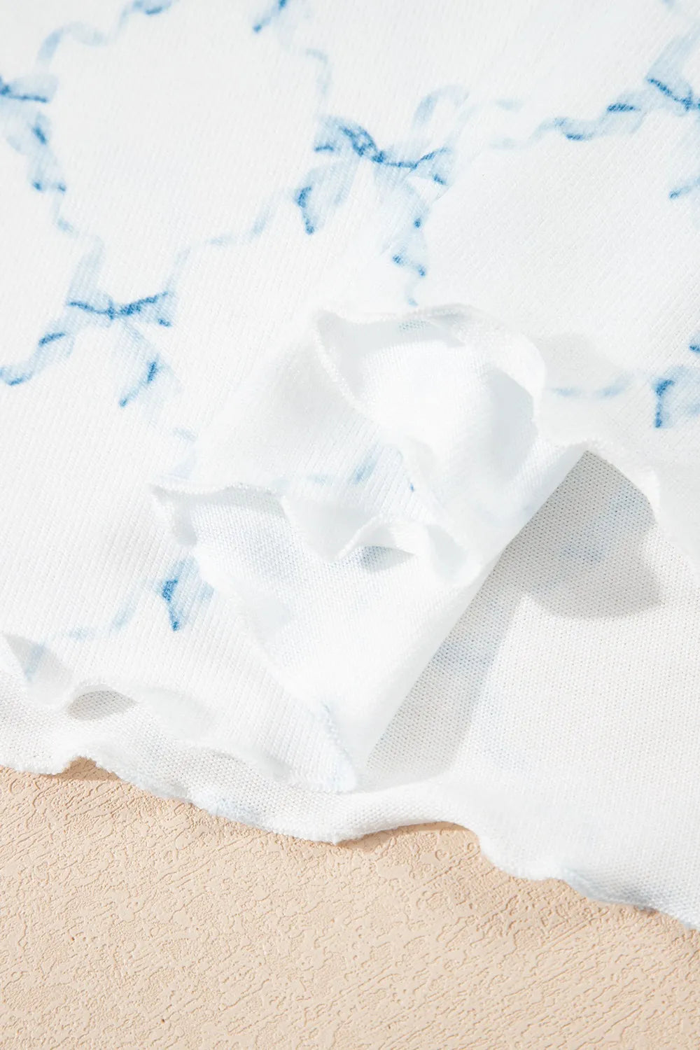 Close up of white fabric with blue tie-dye print and lettuce trim on the Printed Round Neck Top and Shorts