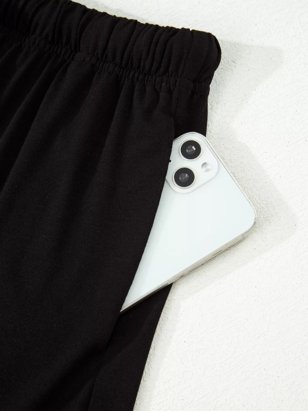Black drawstring shorts with a white smartphone in the pocket