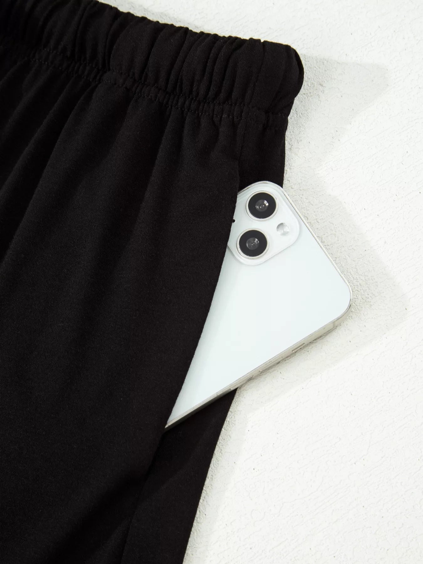 Black drawstring shorts with a white smartphone in the pocket