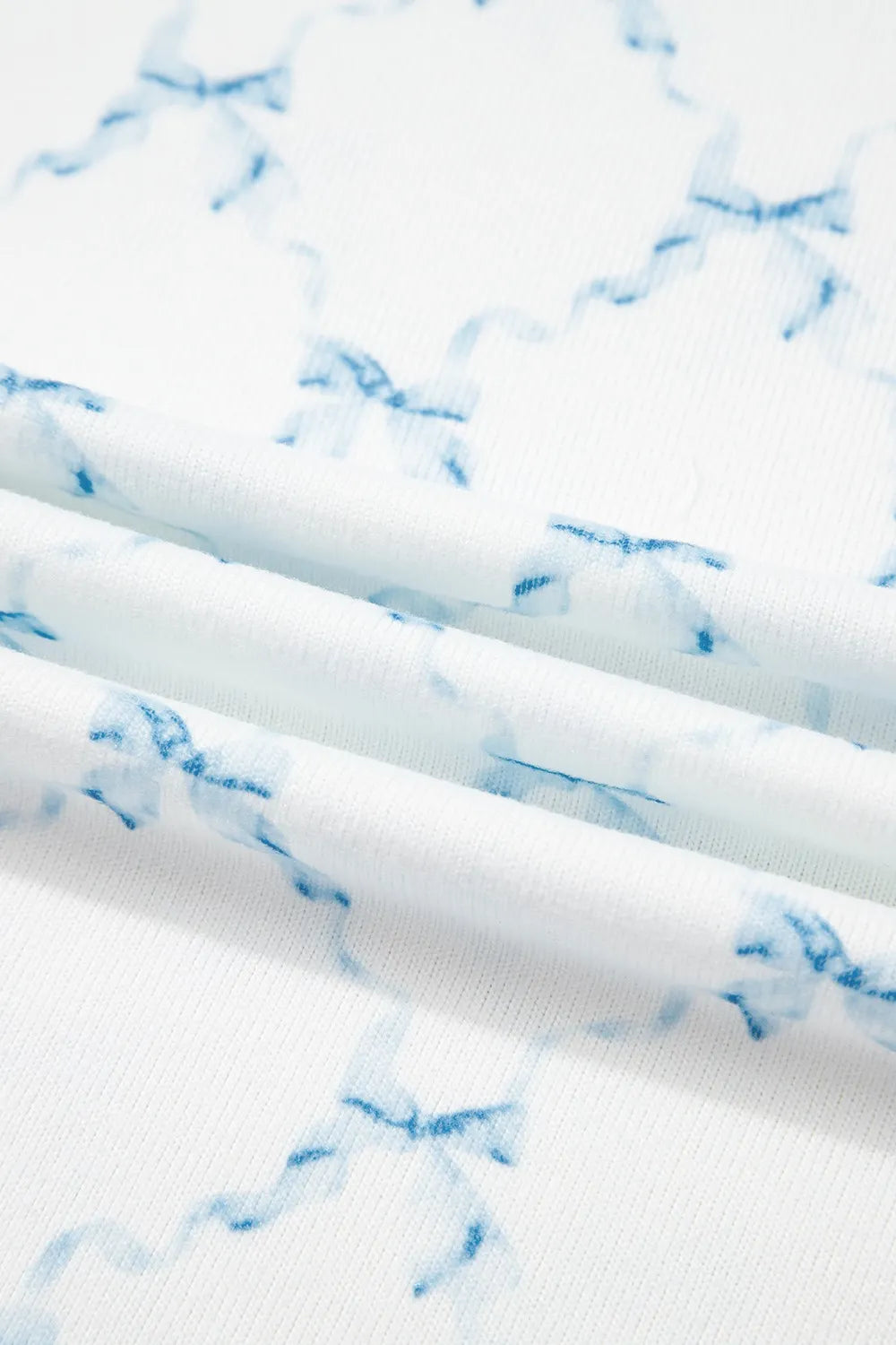 Close-up of white fabric with a blue bow print, part of the Printed Round Neck Top and Shorts Two-Piece Lounge Set