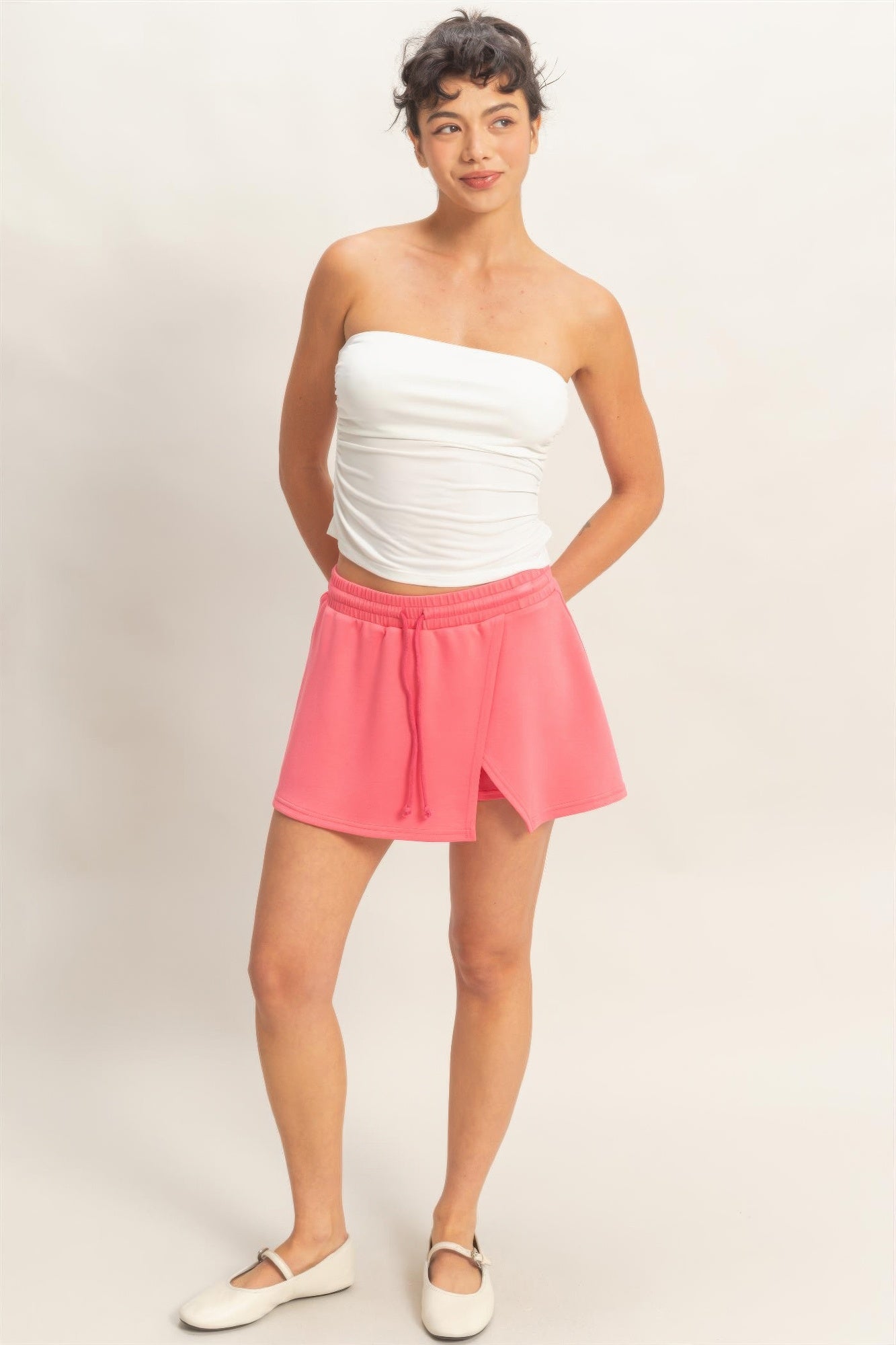 Woman wearing a white strapless top and a Coral Blush Wrap Skort with a drawstring waist