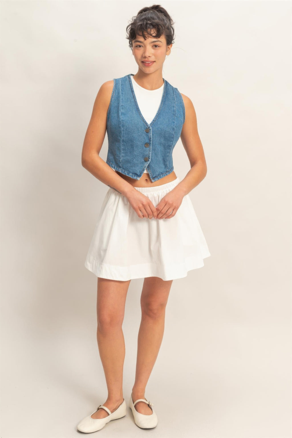 Washed Indigo Denim Button-Front Cropped Vest worn by a woman with a white top and skirt