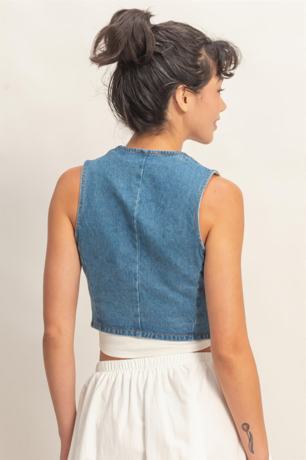 Back view of a woman wearing a Washed Indigo Denim Button-Front Cropped Vest over a white top and white skirt