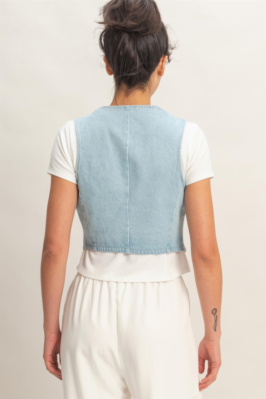 Back of a woman wearing a Washed Sky Denim Button-Front Cropped Vest over a white t-shirt and white pants