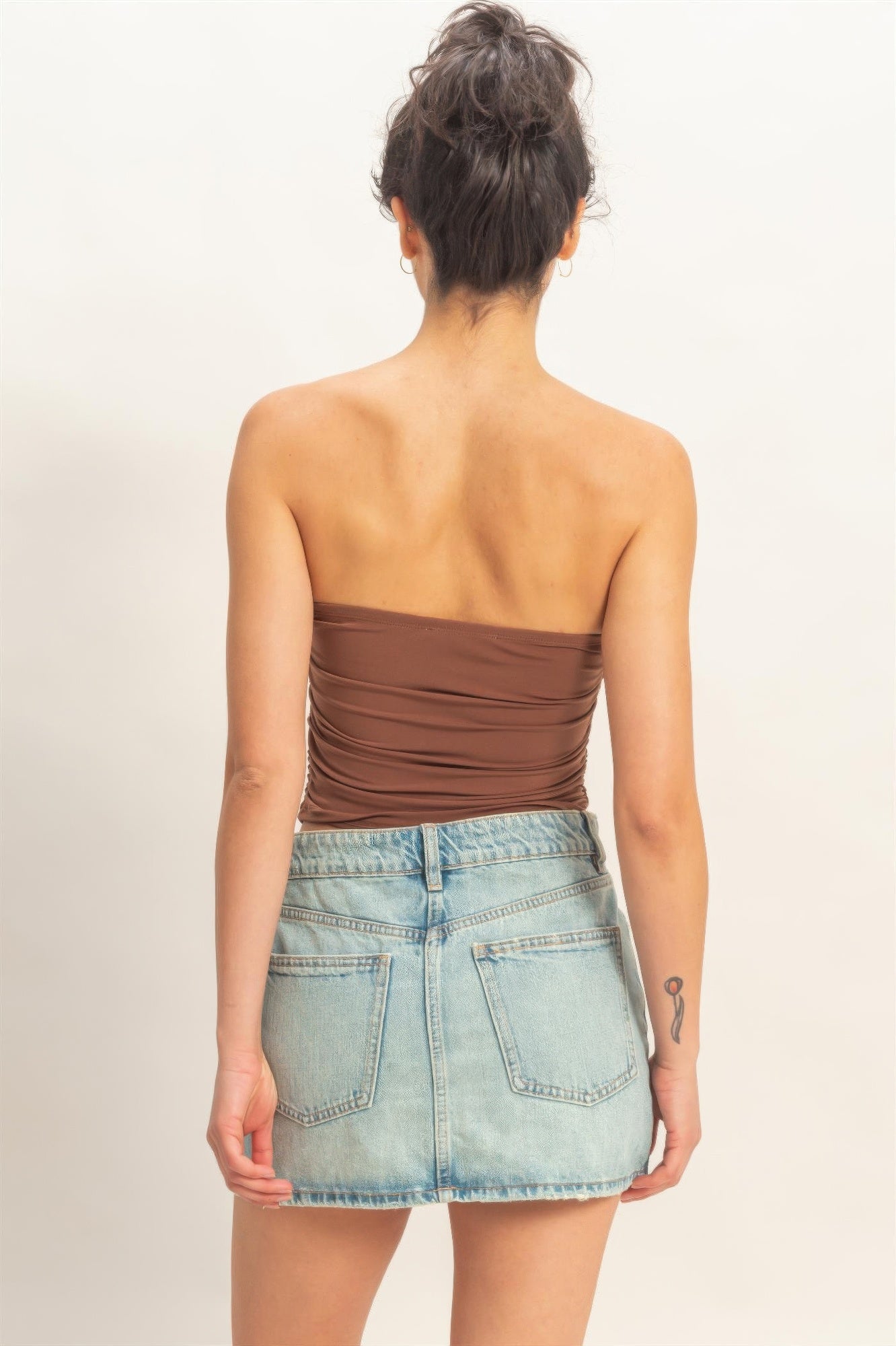 Rear view of model wearing Cocoa Truffle Ruched Strapless Bodycon Top and light wash denim skirt