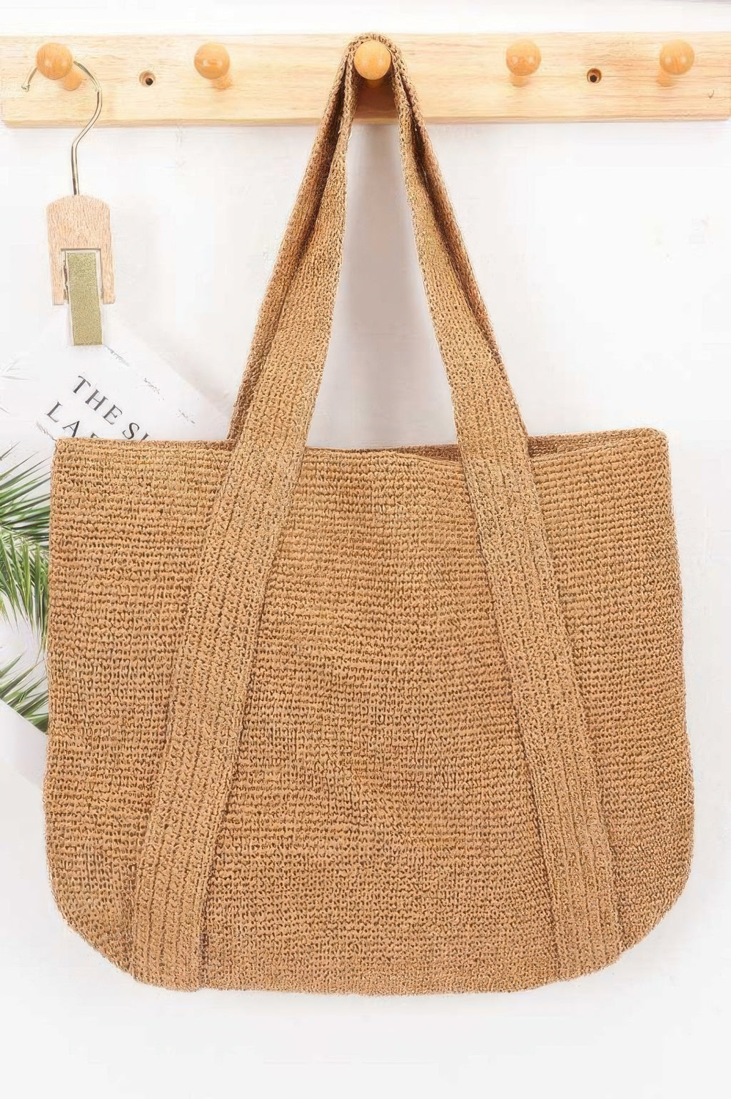 Woven Straw Tote Bag hanging on a wooden hook against a white wall