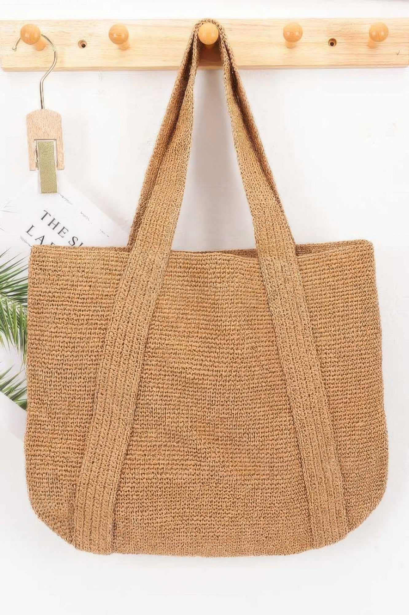 Woven Straw Tote Bag hanging on a wooden hook against a white wall