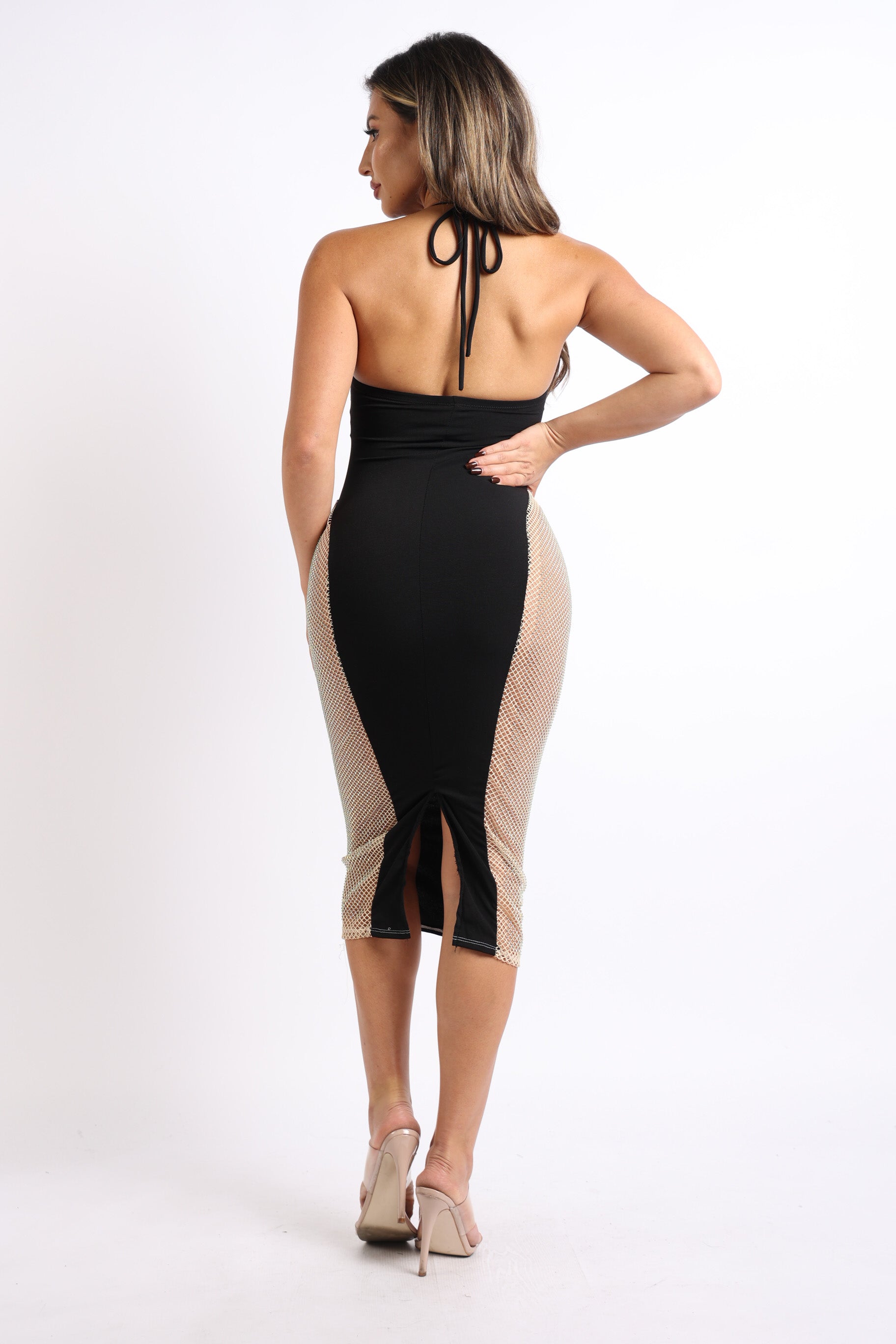 Back view of a woman in a black halter dress with rhinestone fishnet side panels and a back slit